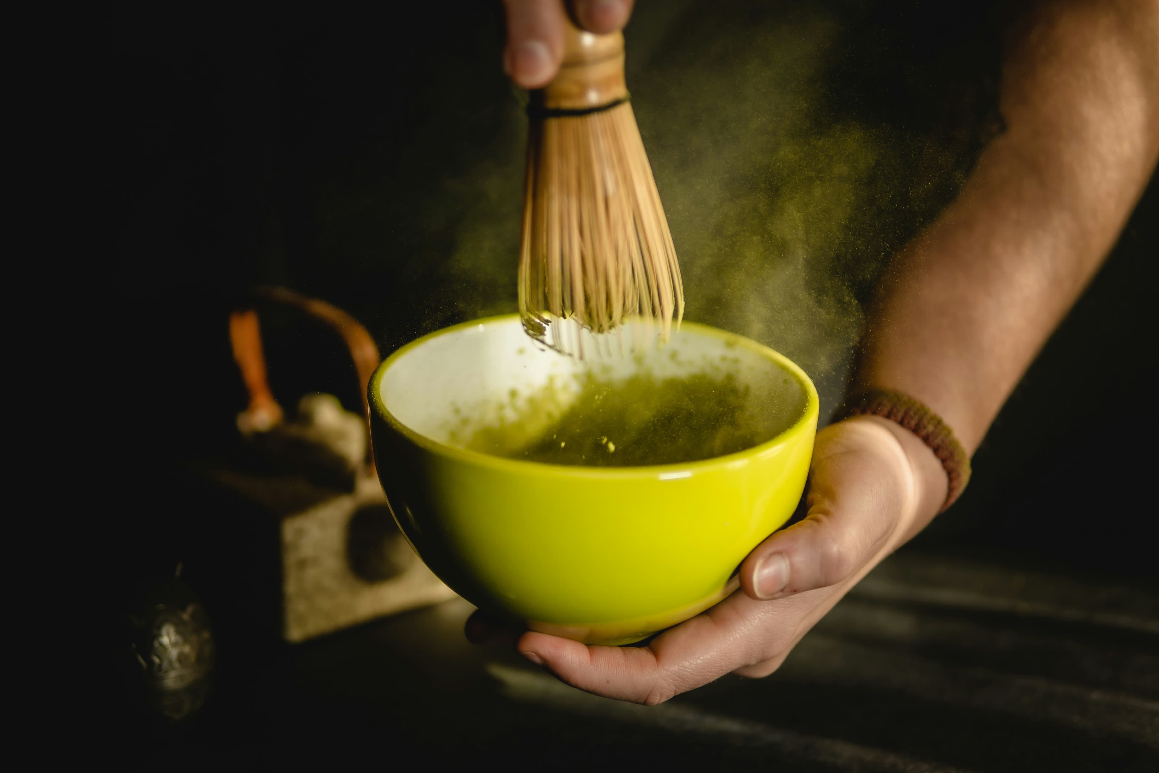 Hands preparing matcha in a yellow ceramic bowl (illustrative image)