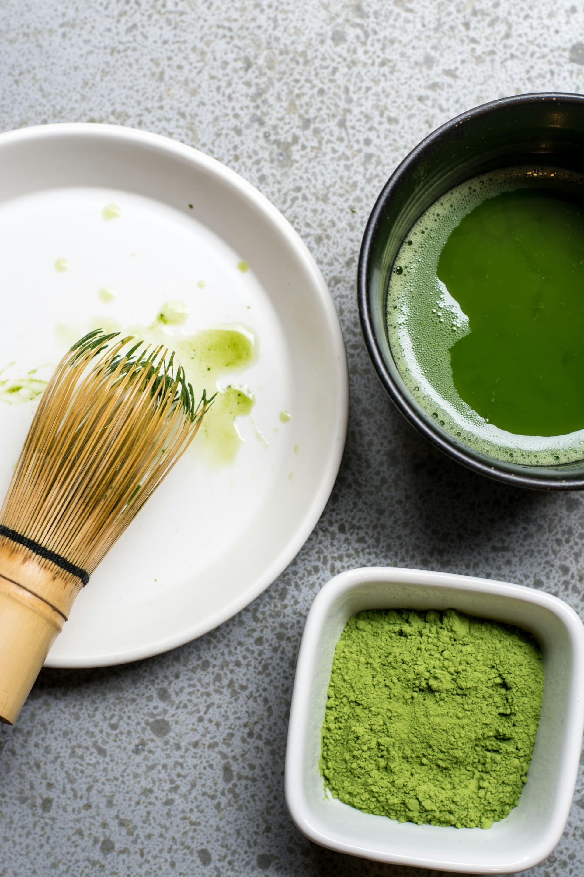 An overhead view of a chasen whisk, matcha bowl, and bright green matcha powder (illustrative image)